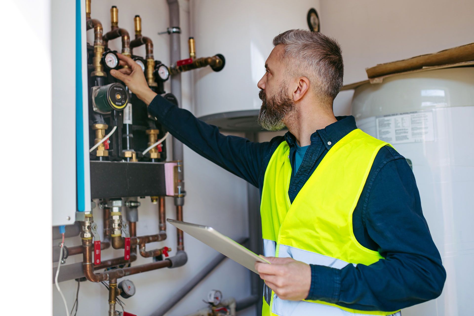 Technician checking boiler gauges while holding a clipboard in utility room. Technician checking boiler gauges while holding a clipboard in utility room.