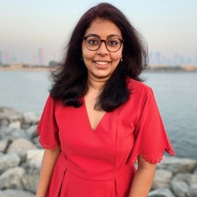 A woman in a red dress and glasses is standing in front of a body of water.