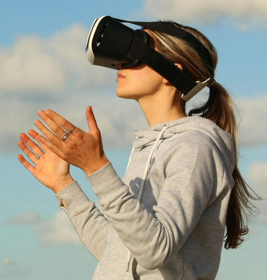 Woman wearing VR headset, hands up, outdoors with blue sky.
