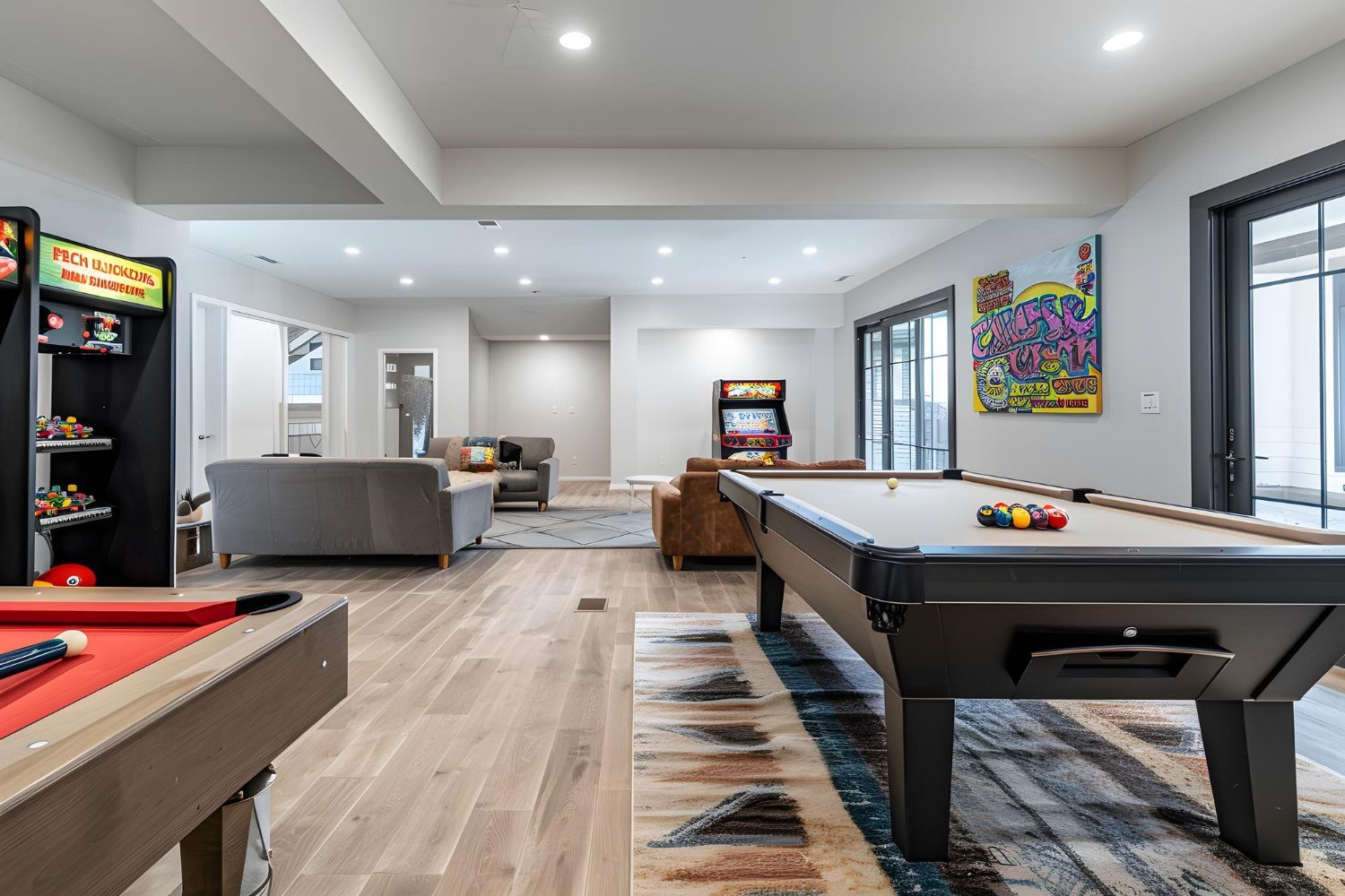 Spacious game room with a pool table, arcade games, and seating area with a colorful rug.
