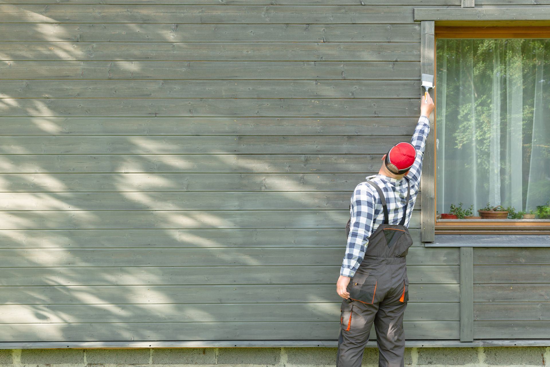 A man is painting the side of a house with a brush.