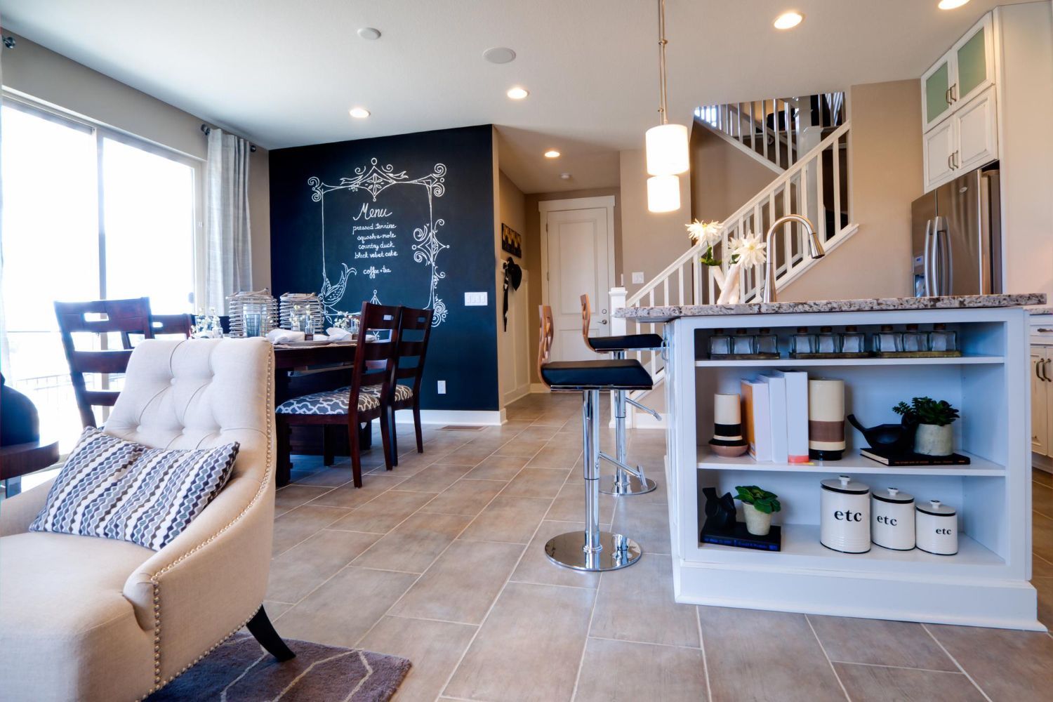 Open-concept kitchen and dining area featuring a chalkboard wall, a breakfast bar, and a tufted armchair in the foreground.
