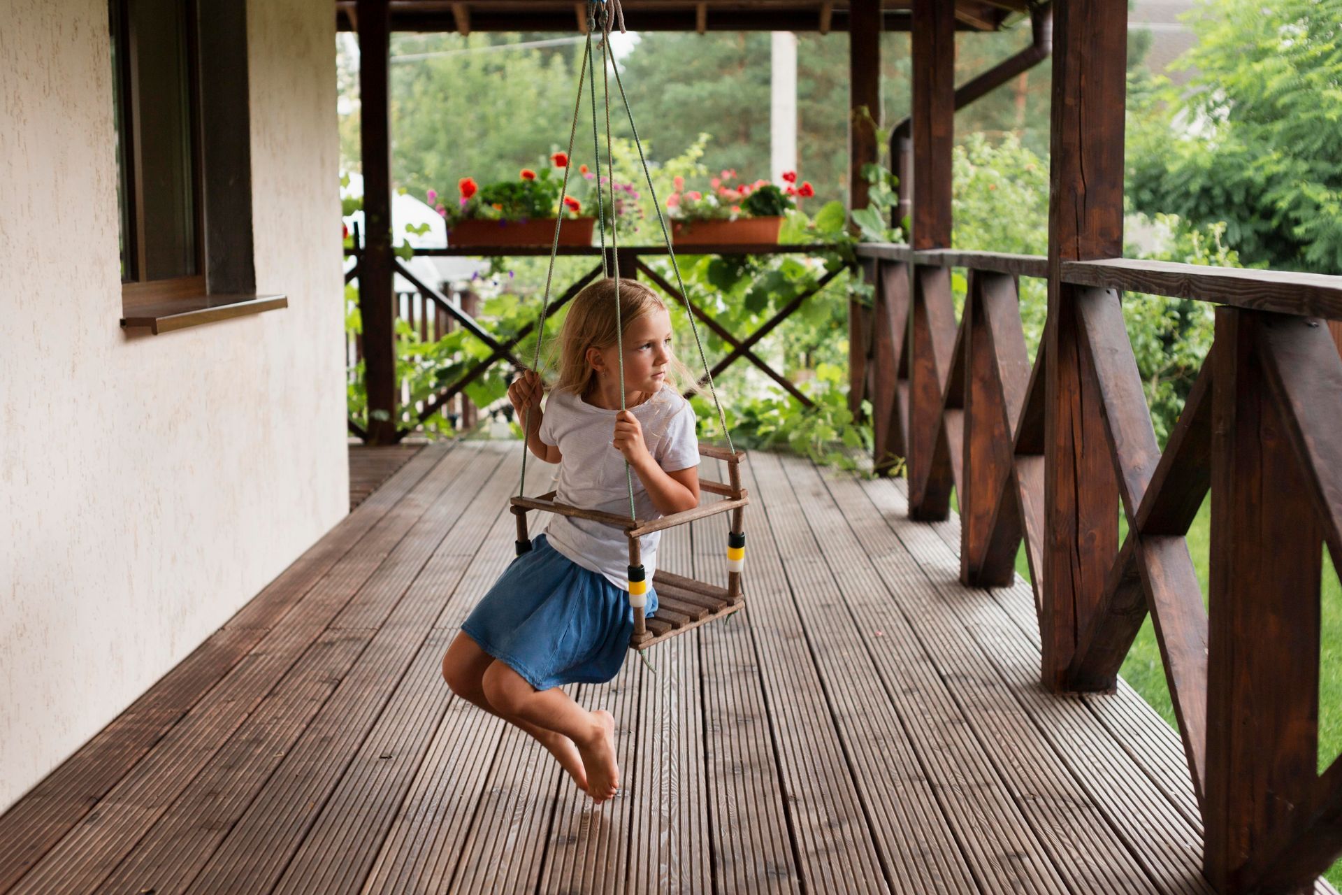 A little girl is sitting on a wooden swing on a porch.
