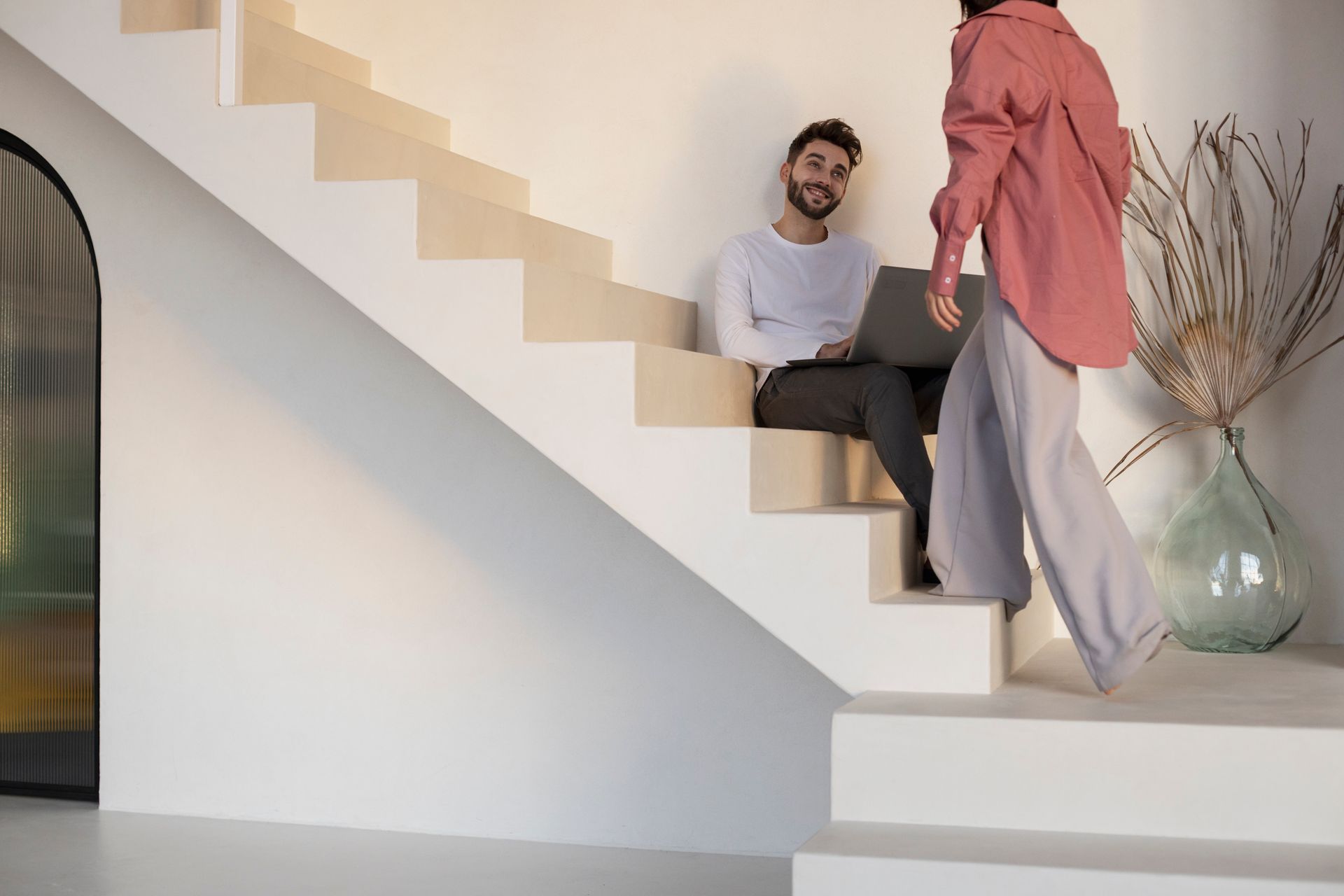 A man and a woman are sitting on the stairs using laptops.
