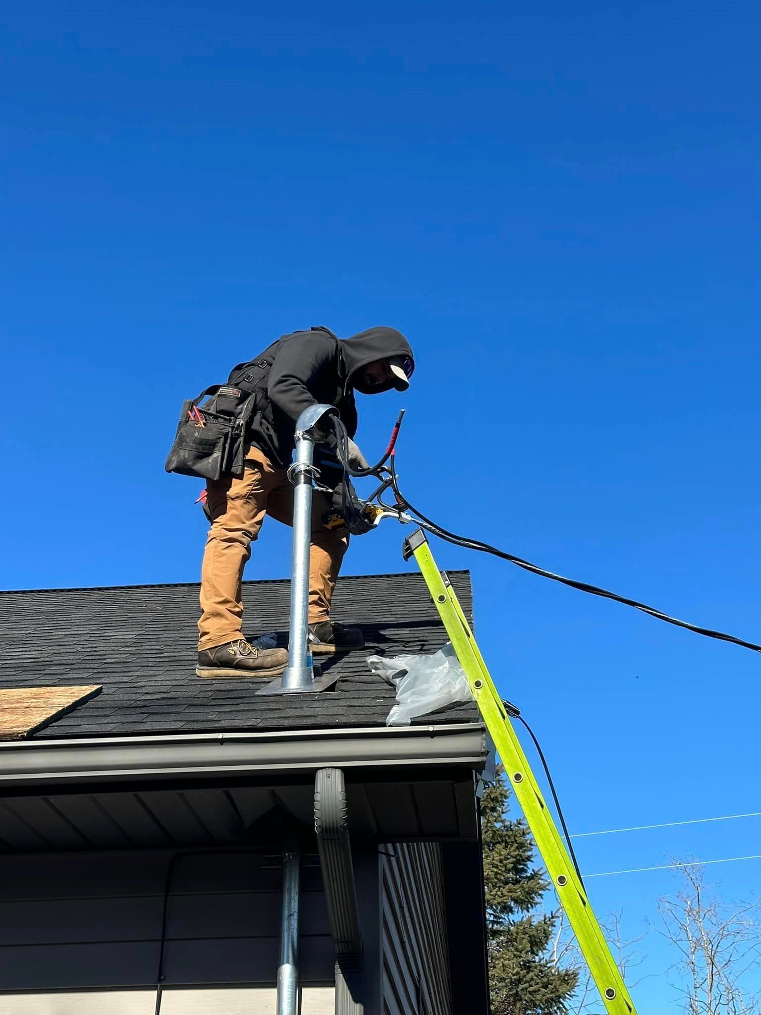 A man is standing on top of a roof with a ladder attached to him.