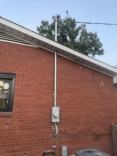 A brick house with a roof and a electrical box on the side of it.