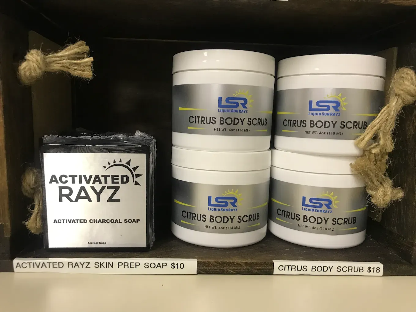 Shelf display with skincare products: soap and body scrubs in white containers.
