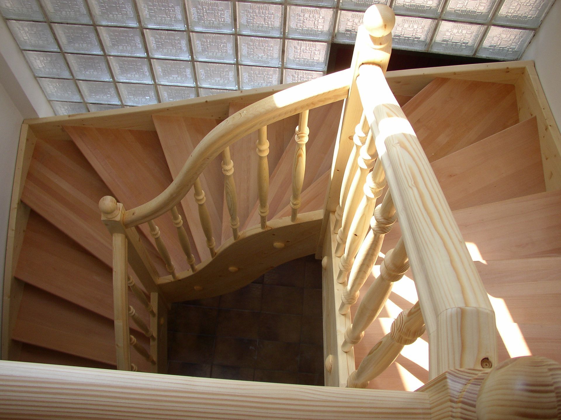 Hölzerne Wendeltreppe mit sonnenbeschienenem Geländer und darüberliegendem Glasbaustein-Oberlicht