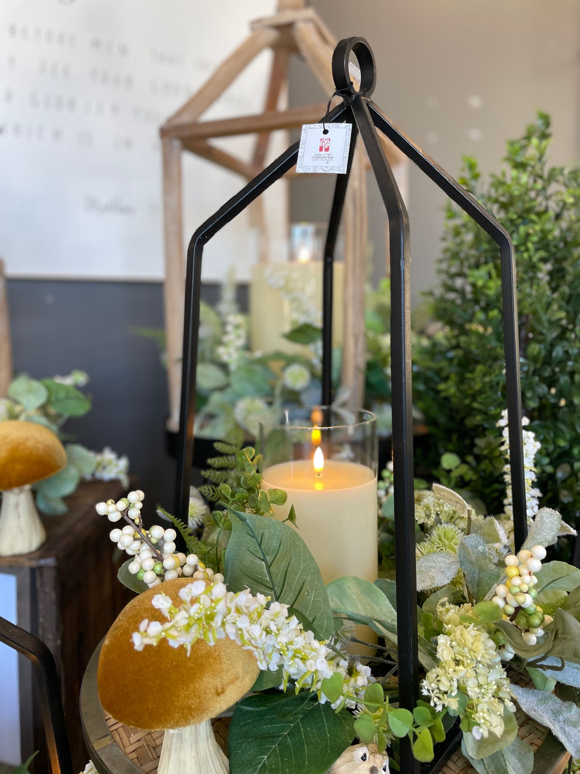 Black lantern with candle, foliage and mushroom decor on a table.