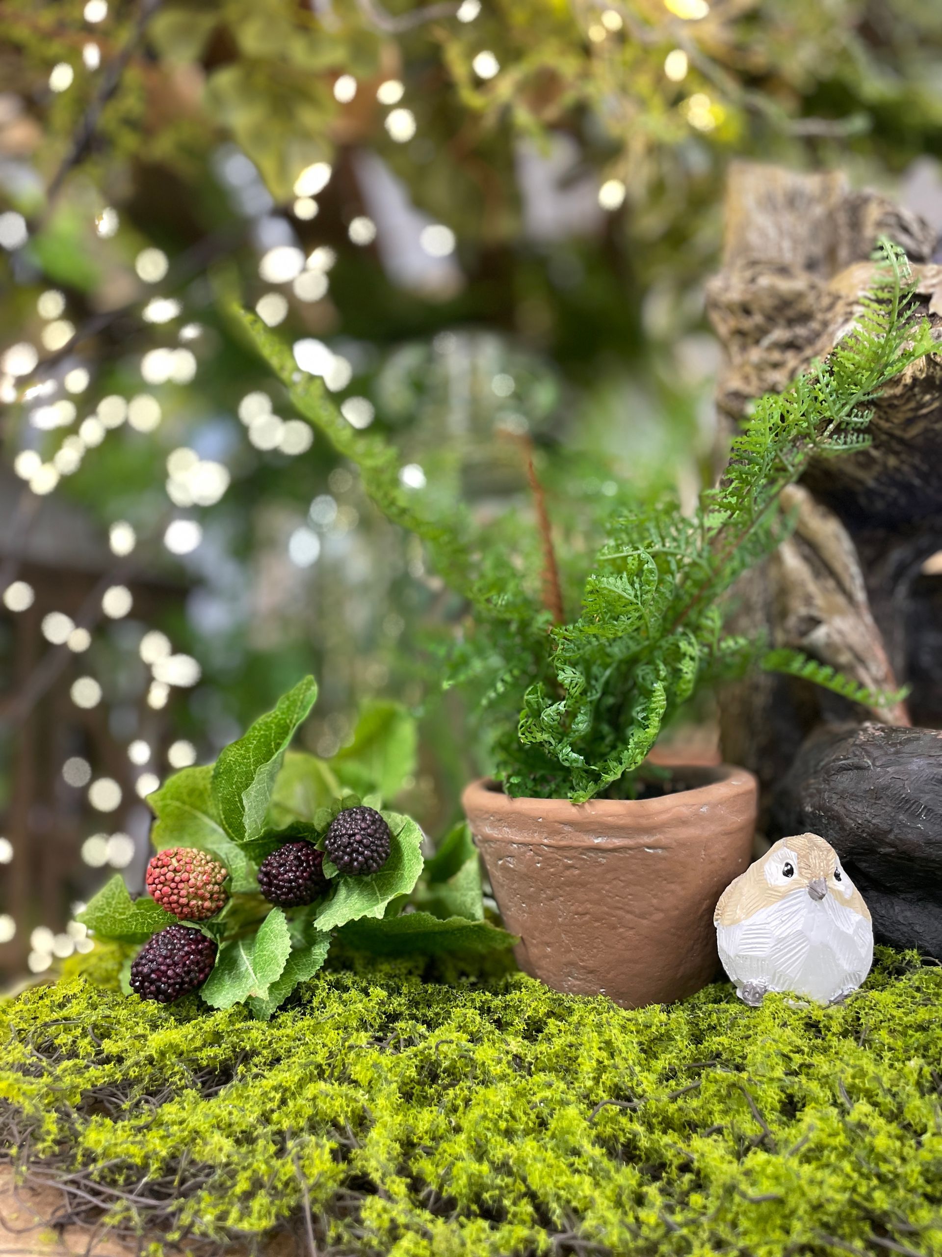 Miniature garden with a potted plant, bird figurine, and berries on moss.