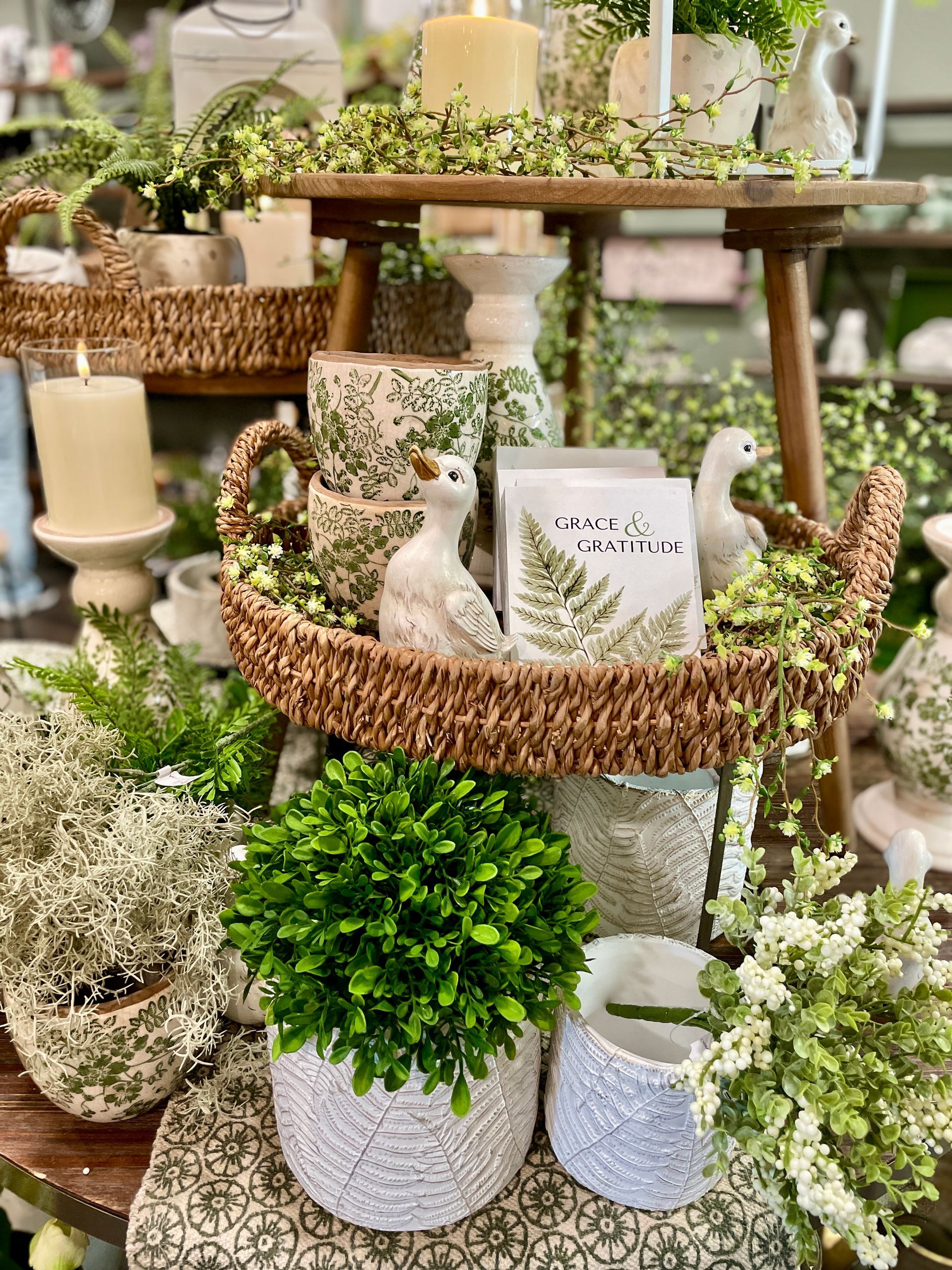 Display of home decor items with candles, greenery, and ceramic pots on a wooden stand.