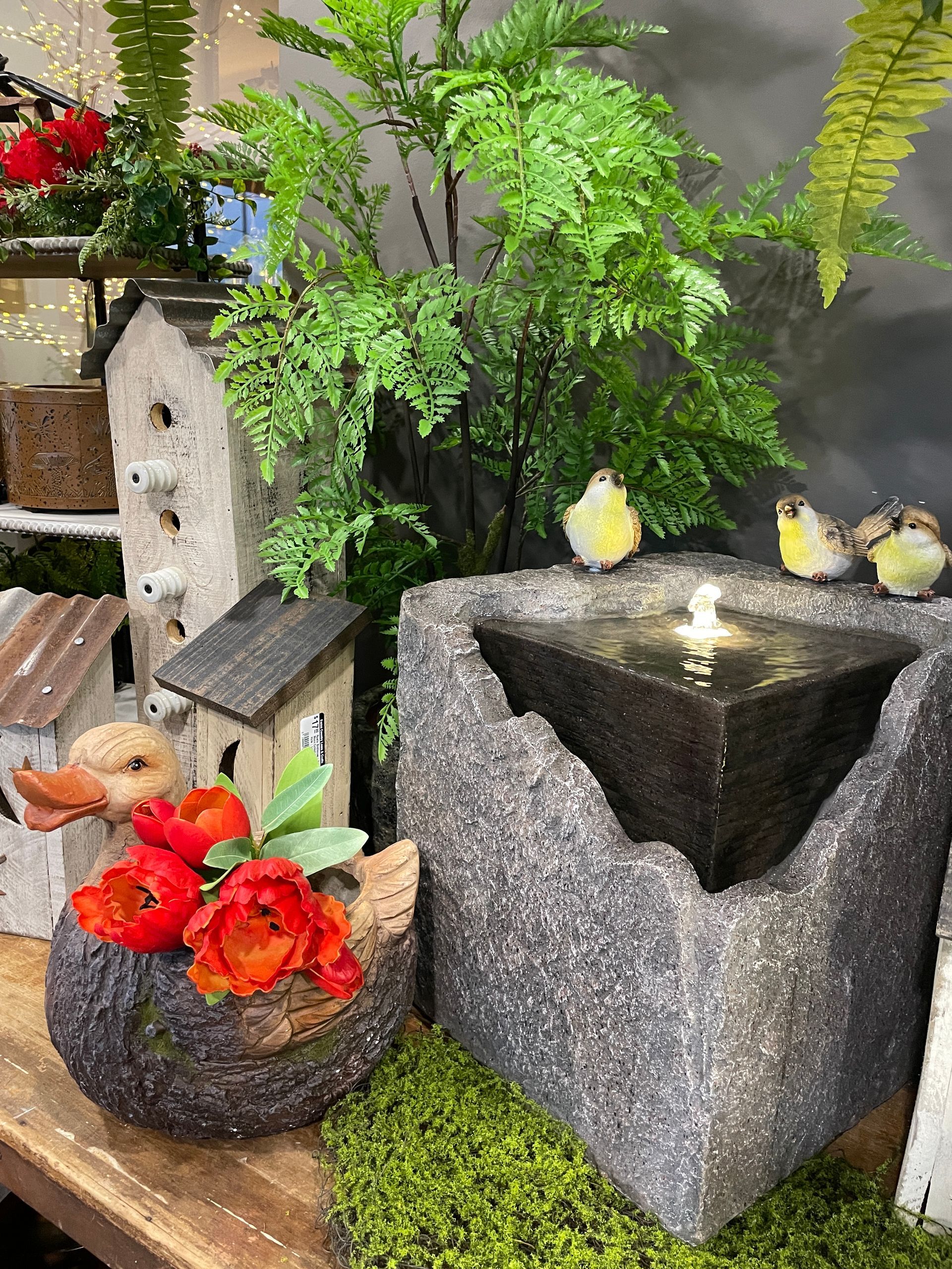 Birdbath with birds, birdhouses, flowers, and greenery arranged on a wooden table.