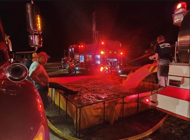 A group of firefighters are working around a water drop tank being filled by fire tanker trucks.