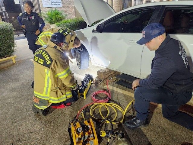 Two firefighters are working on a car with the hood open.