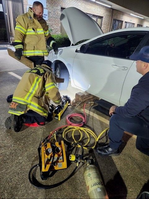 A group of firefighters are working on a car in a parking lot.