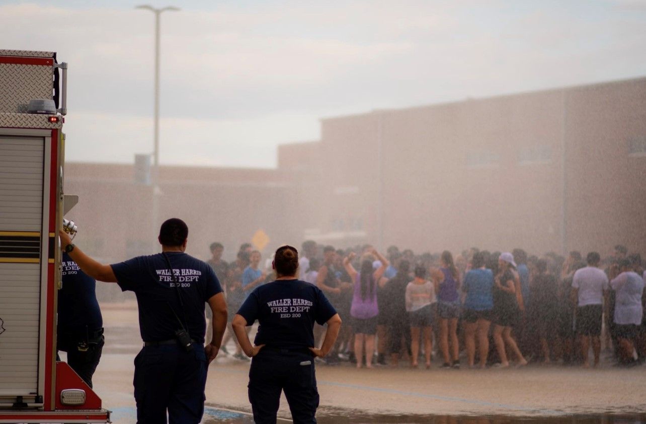 A group of school students are being sprayed by a fire truck.