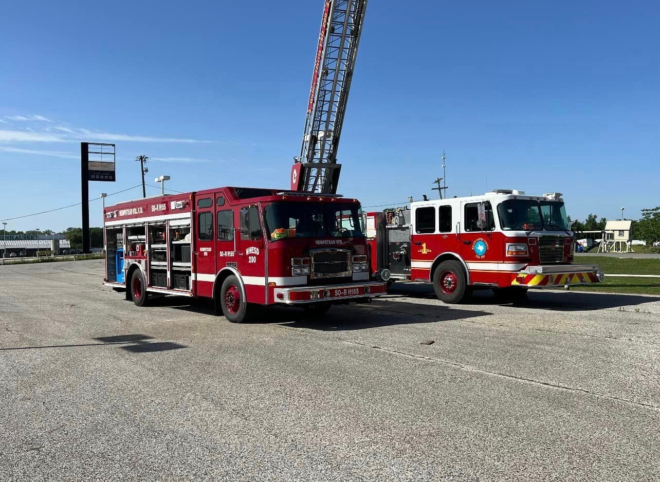 Two red fire trucks are parked next to each other in a gravel lot.