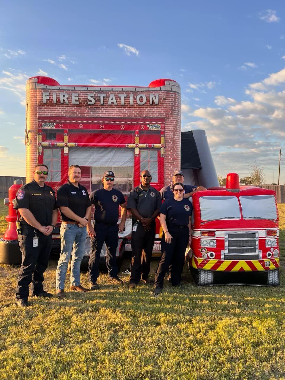A group of firefighters are posing for a picture in front of a fire station.