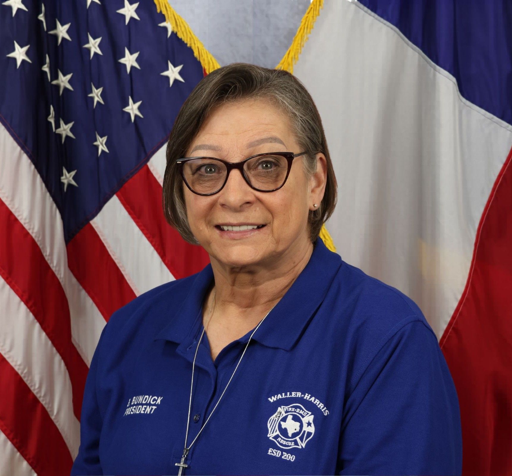 A picture of Commissioner Brenda Bundick  wearing a gray shirt while standing in front of an American flag.