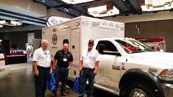 Three men are standing next to an ambulance in a room.