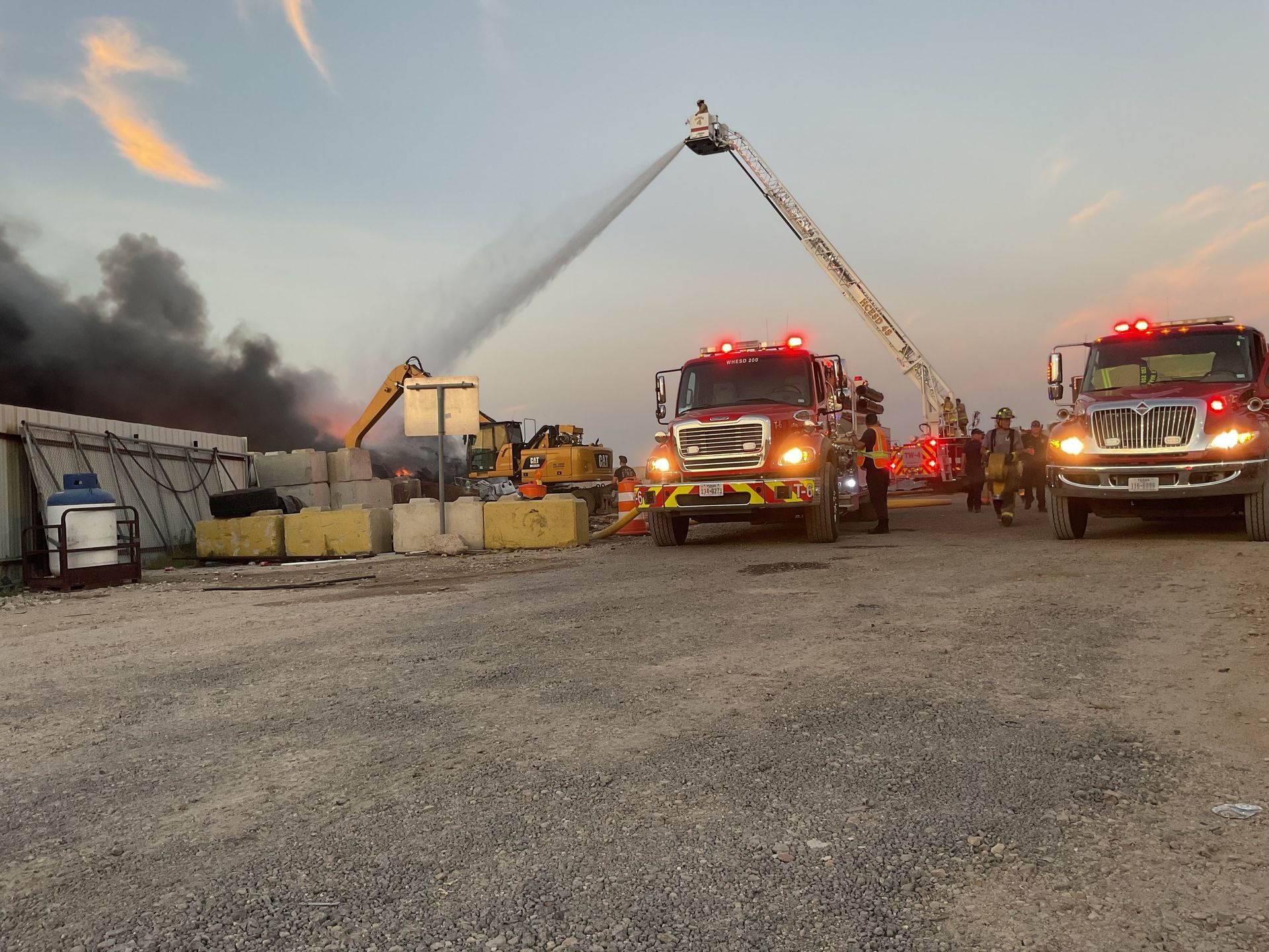 A group of fire trucks are parked in a gravel lot
