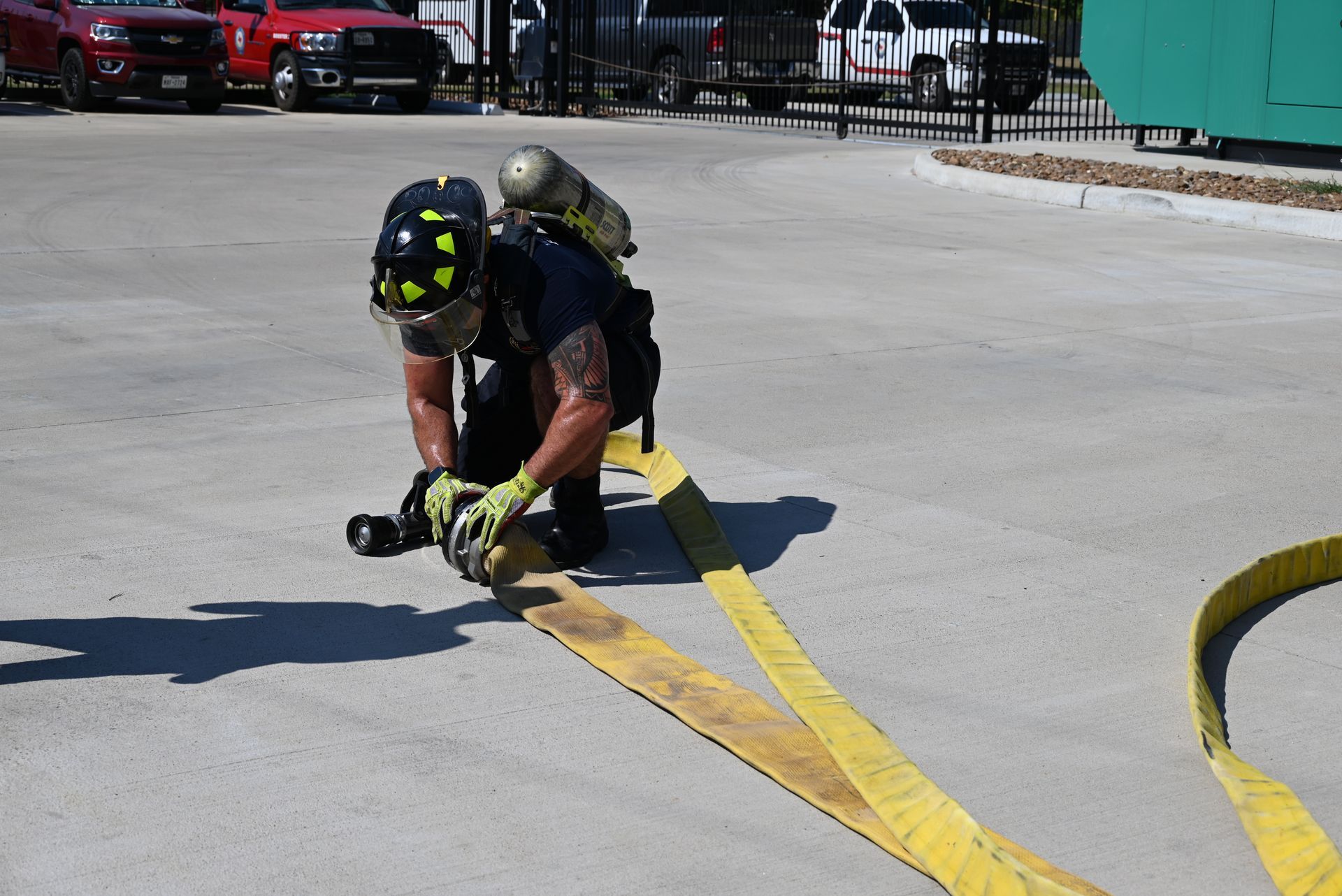A firefighter is kneeling down on the ground holding a fire hose.