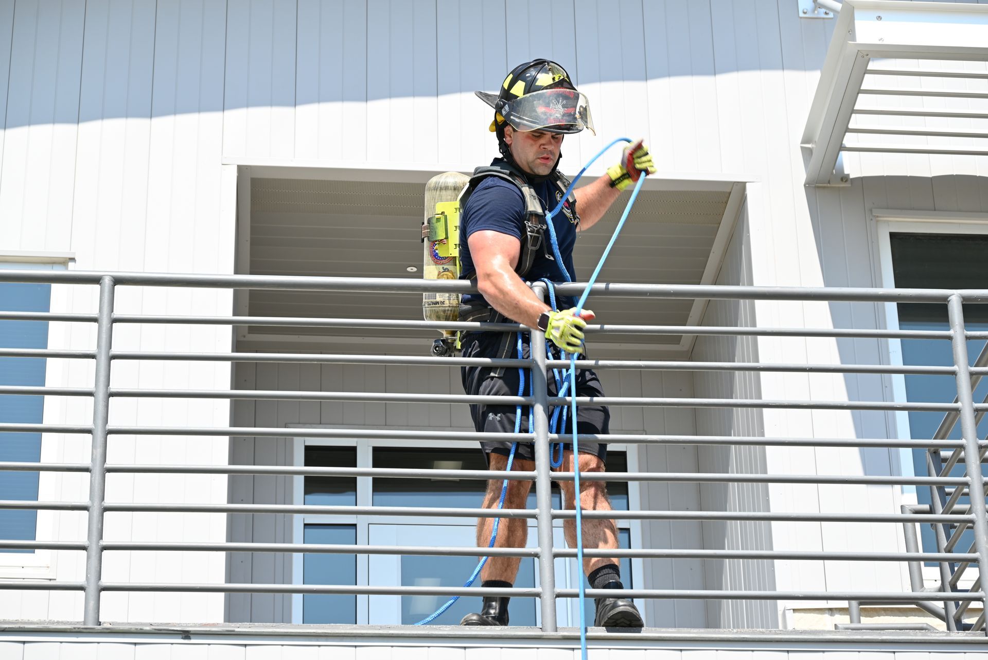 A firefighter is standing on a balcony holding a rope.