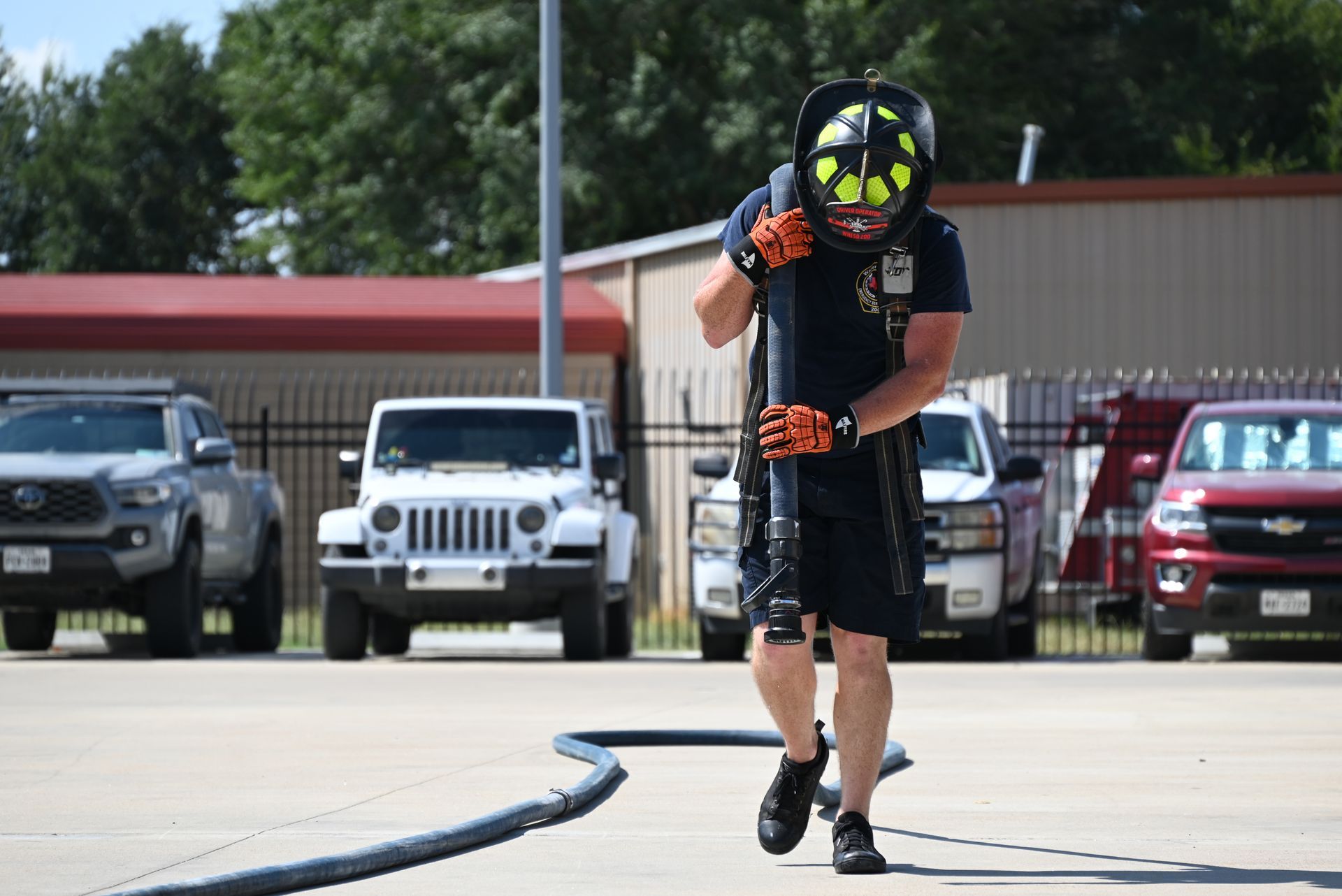 A firefighter is running with a hose in a parking lot.