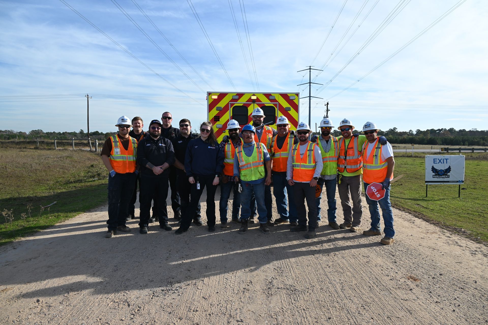 A group of construction workers are posing for a picture in front of an ambulance.