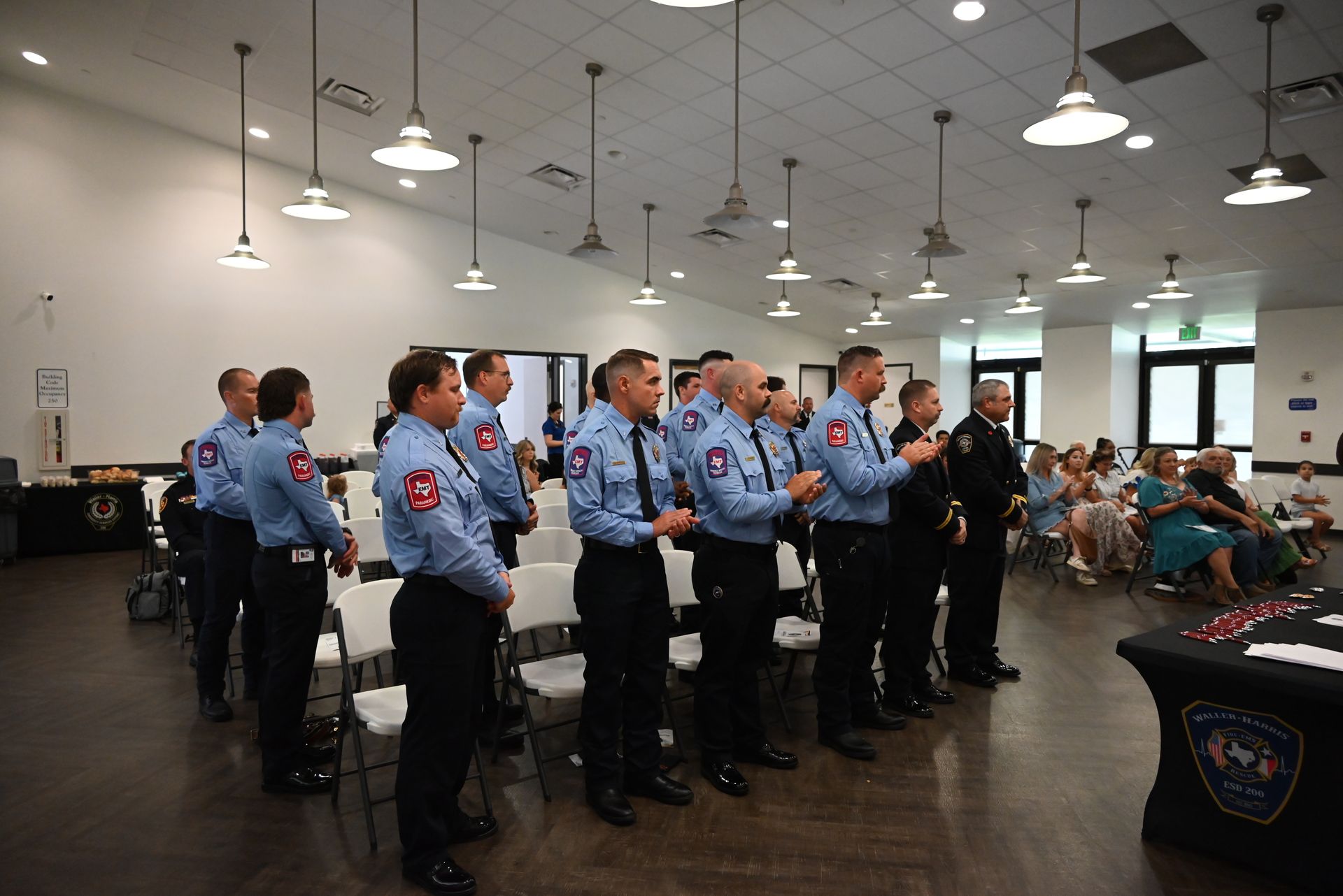 Photo of badge pinning ceremony participants, firefighters dressed in class A uniforms standing while clapping.