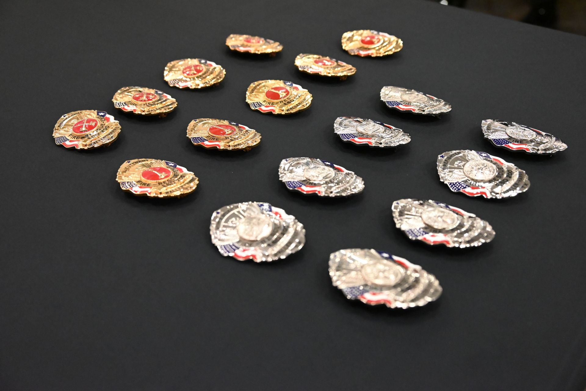 Photo of fire department badges place on a black table lined up in a row in order by rank.