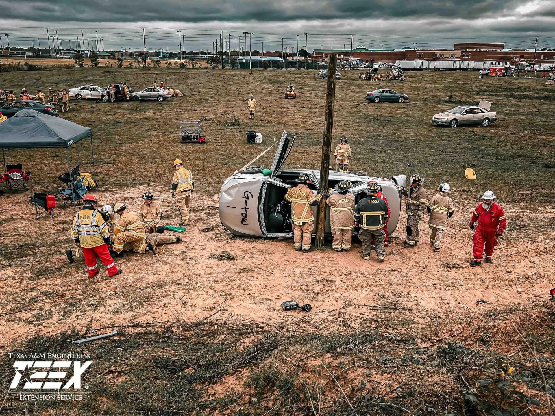 A group of firefighters are standing around a car that is on its side during a training class. 