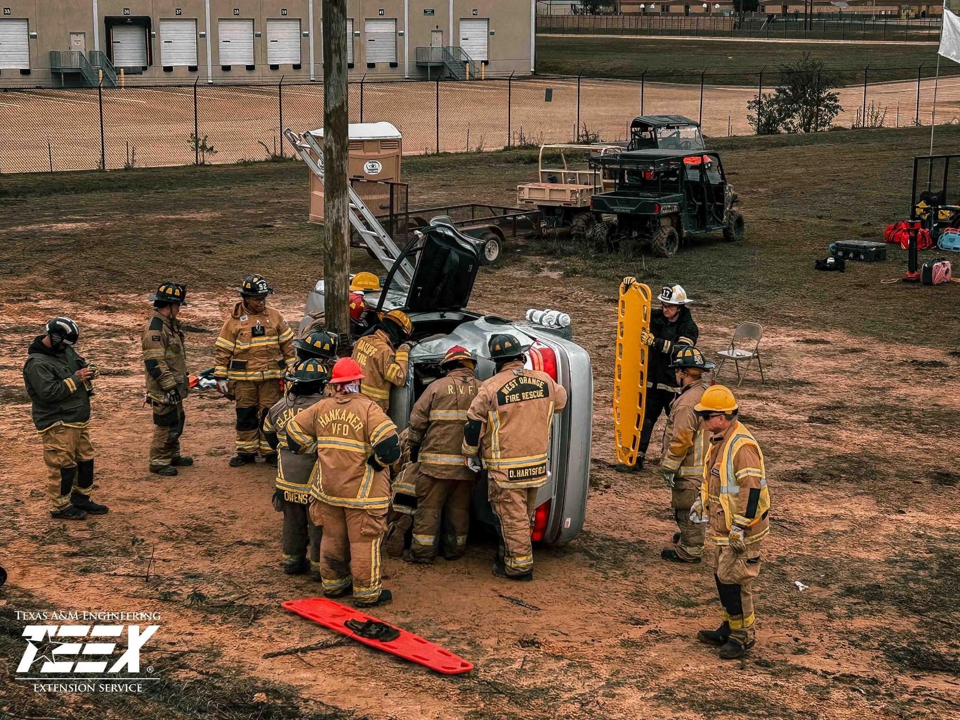 A group of firefighters are standing around a car that is on its side during a training class. 