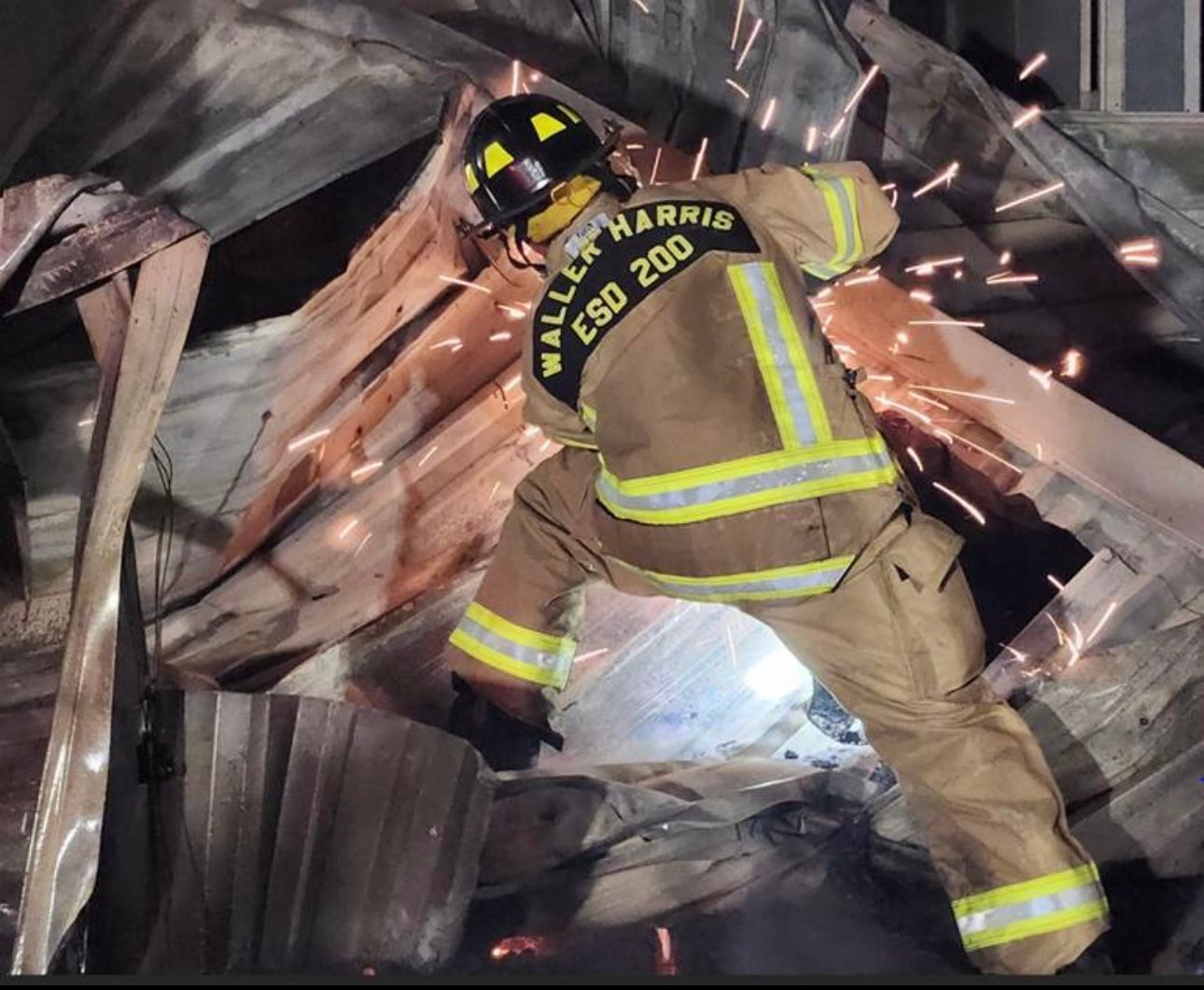 A fire fighter kneels by a car spraying water as car is steaming. 