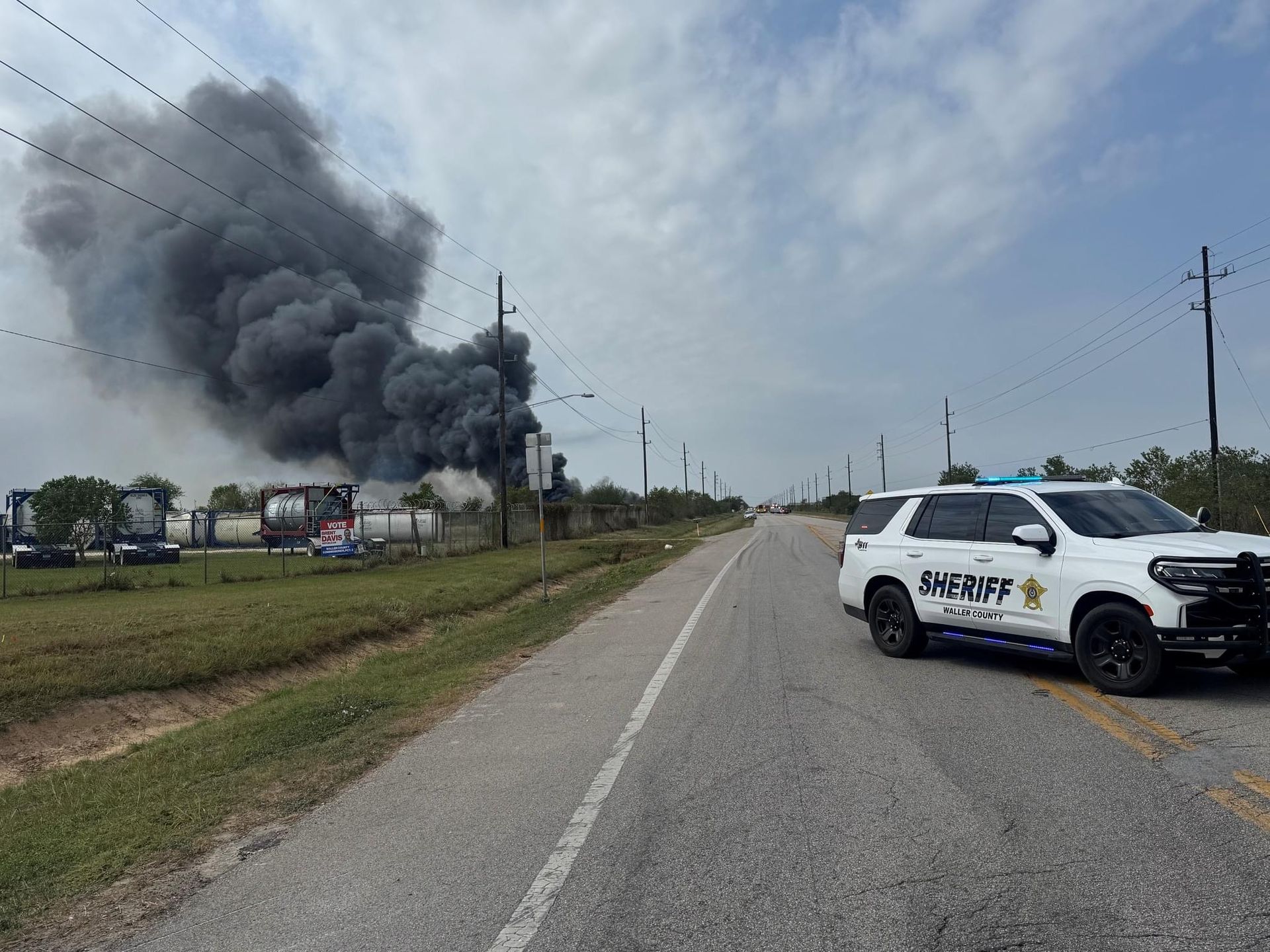 A sheriff 's car is parked on the side of the road in front of a large smoke cloud.