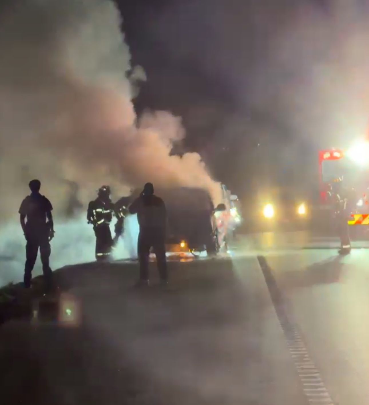 A group of fire fighters are spraying water on a car fire on a highway.