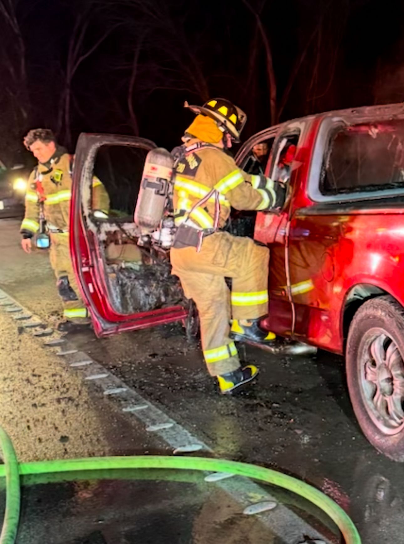 Two fire fighters search a burned vehicle after extinguishment.