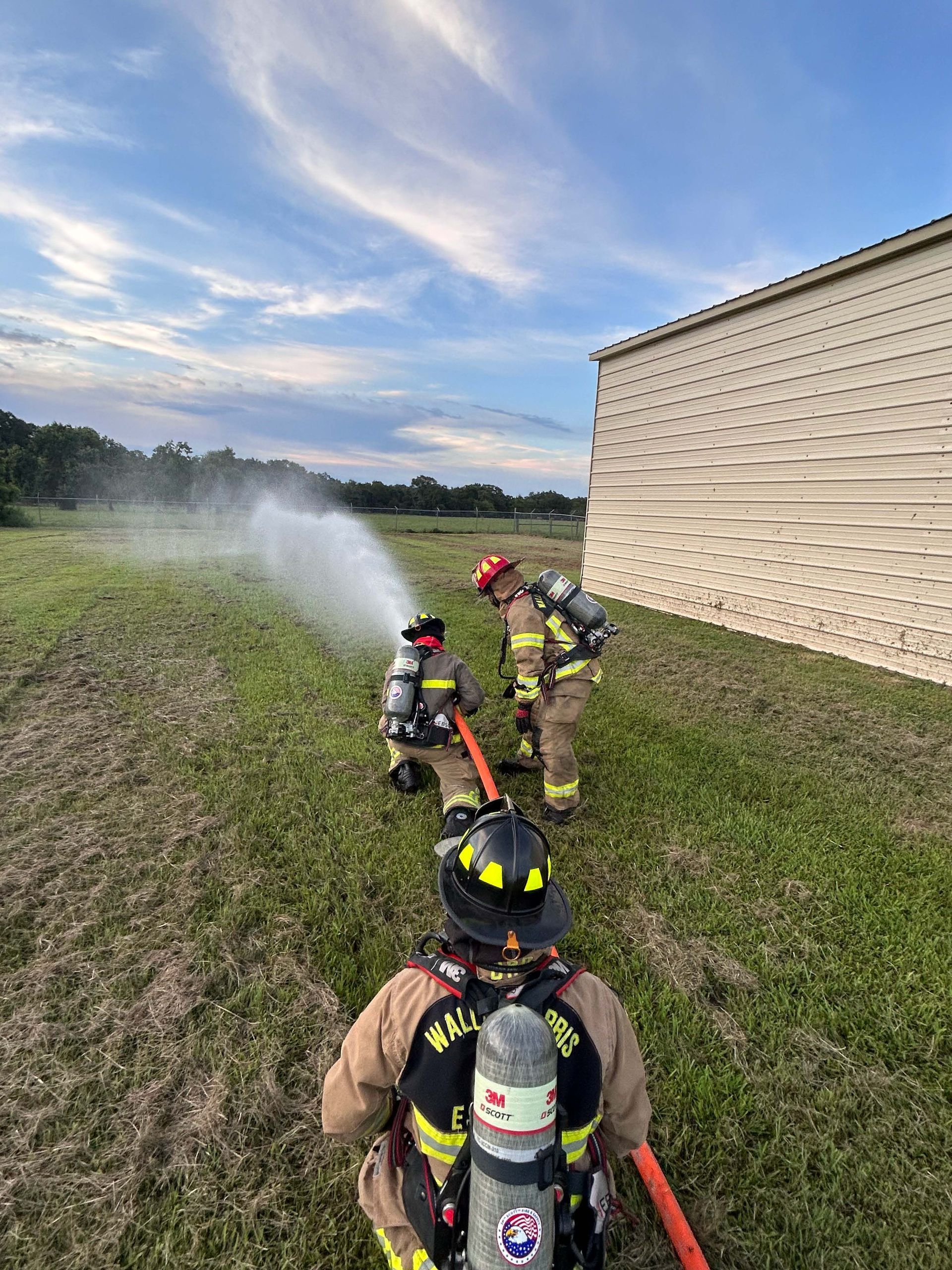 A group of firefighters are spraying water from a hose in a field.