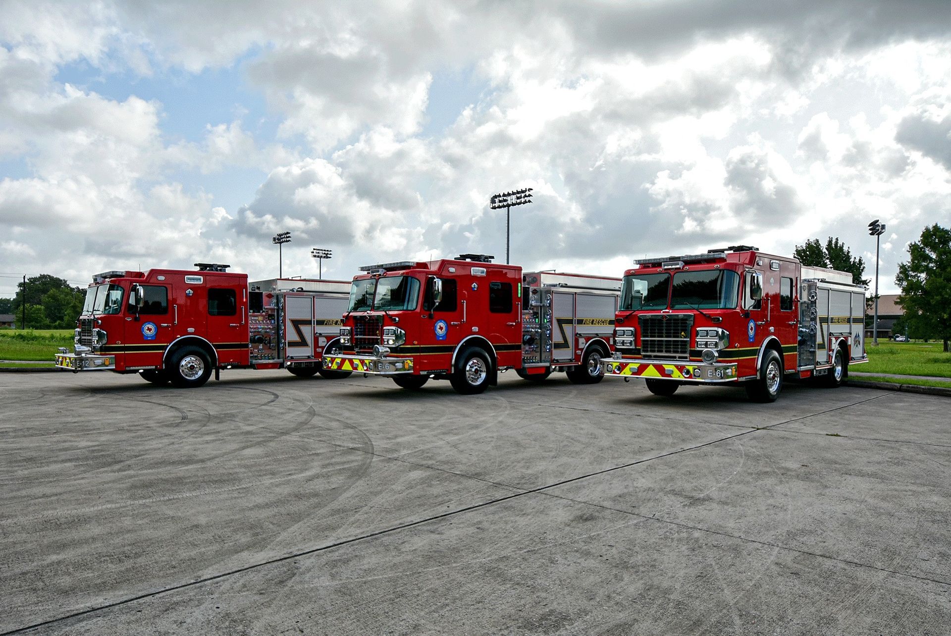 Three fire trucks are parked in a parking lot on a cloudy day.
