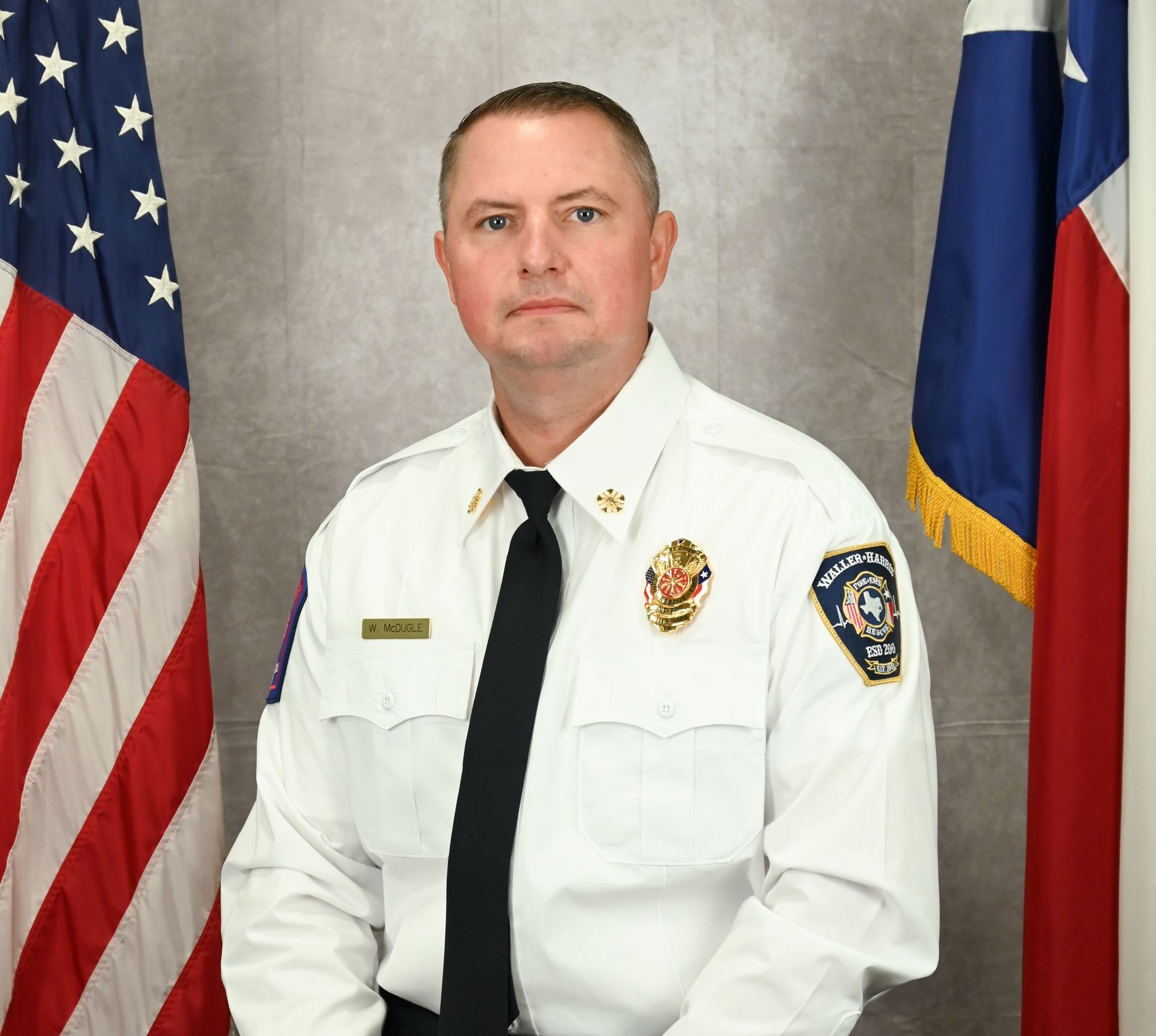 Portrait of Fire Chief William McDugle seated before U.S. and Texas flags.