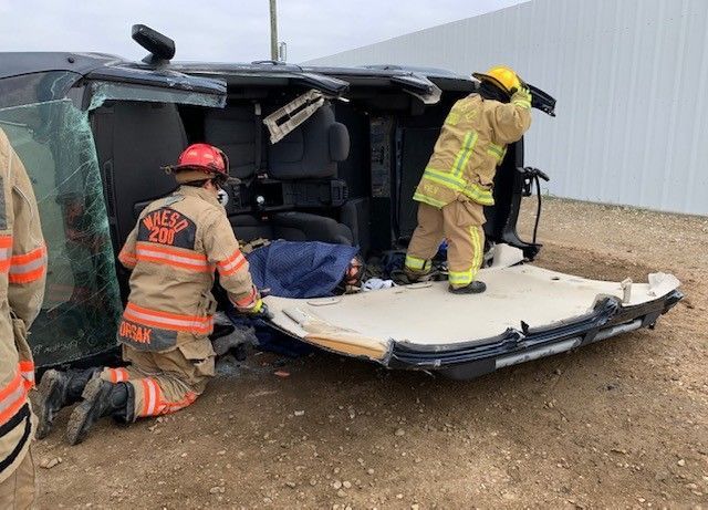 A group of firefighters are working on a car that has turned over.