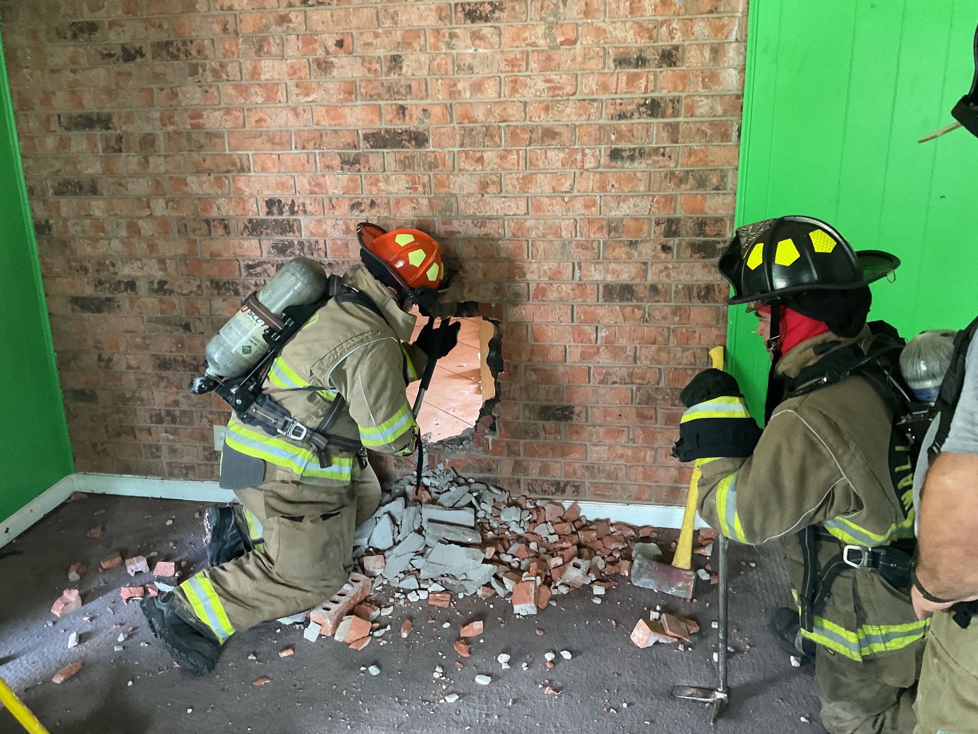 A group of firefighters are breaching a brick wall during a training exercise.