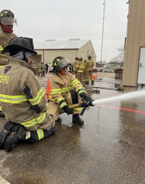 A group of firefighters are kneeling down and using a hose to spray water.