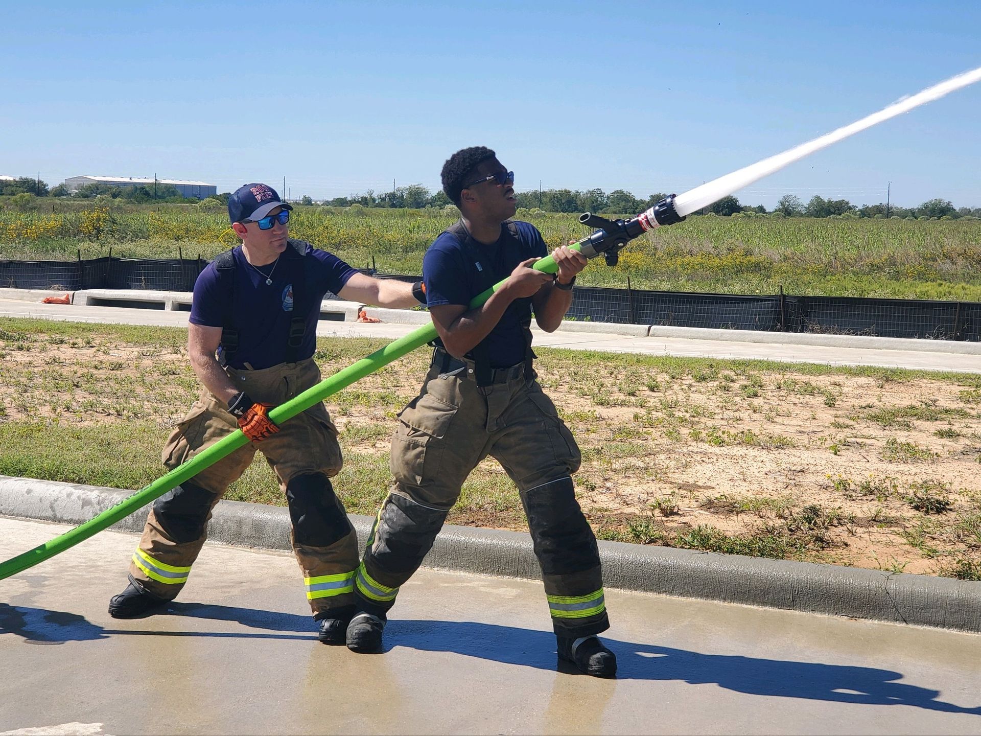 Two firefighters are standing next to each are training with a fire hose.