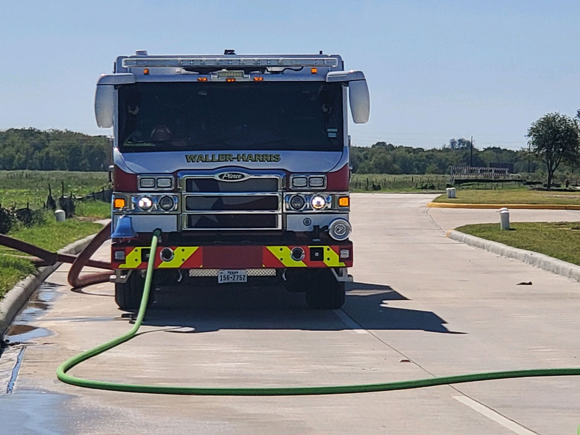 A fire truck is parked on the side of the road with a green hose attached to it.