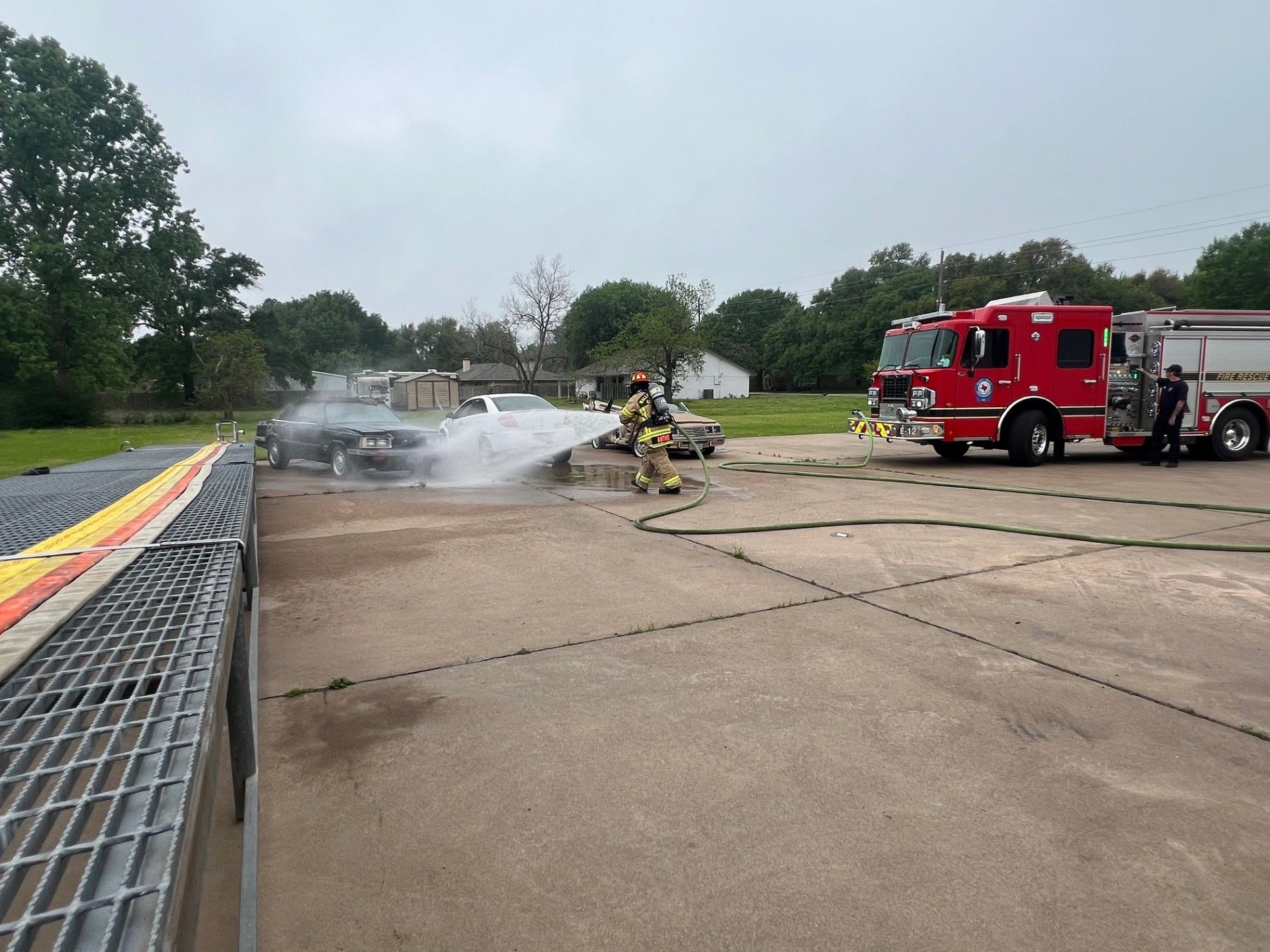 A firefighter is spraying water on a car in a parking lot.