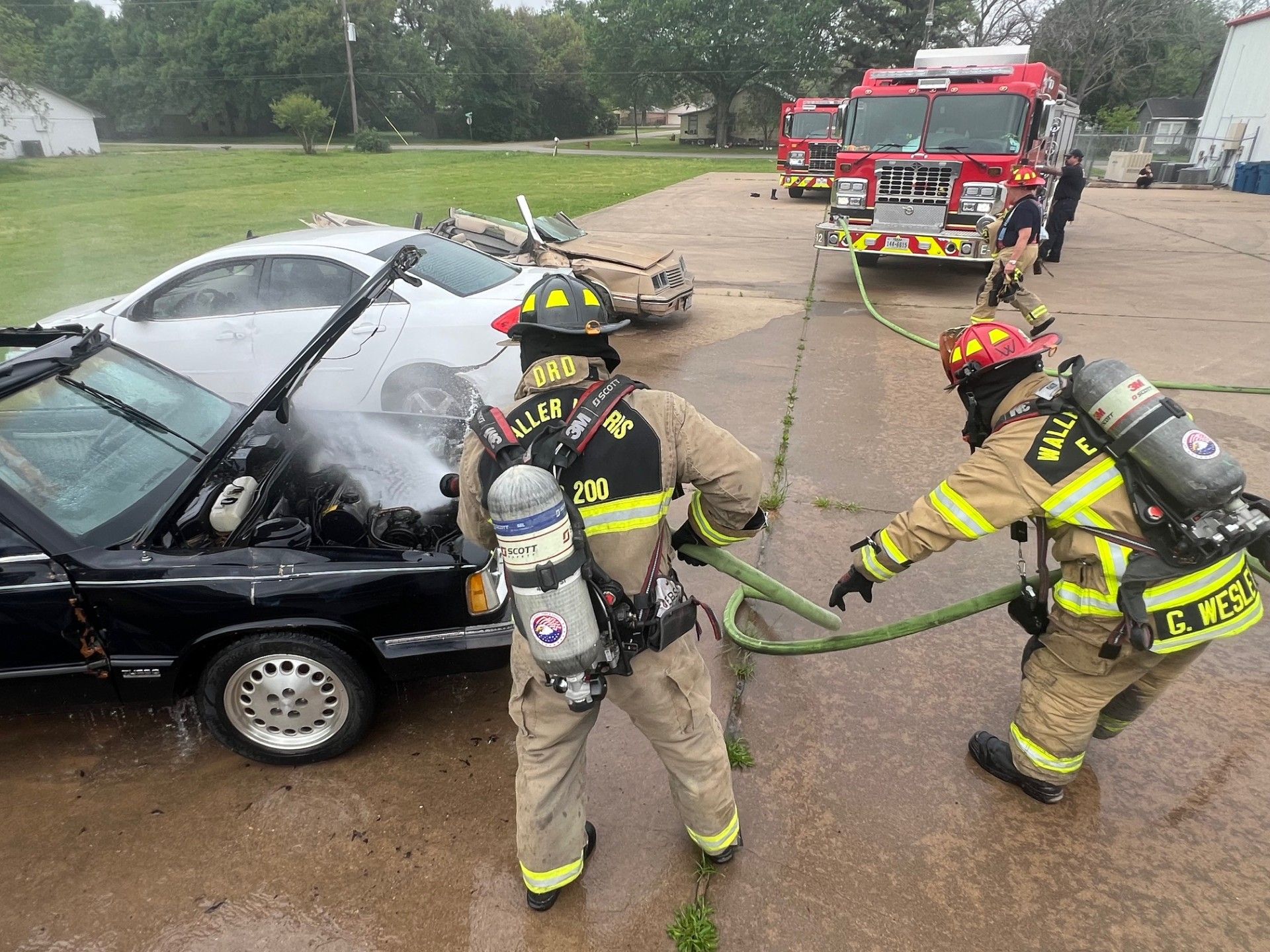 Two firefighters are spraying a car with a hose.