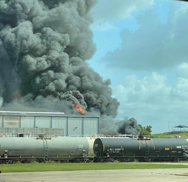 A large cloud of smoke is coming out of a building next to a train.