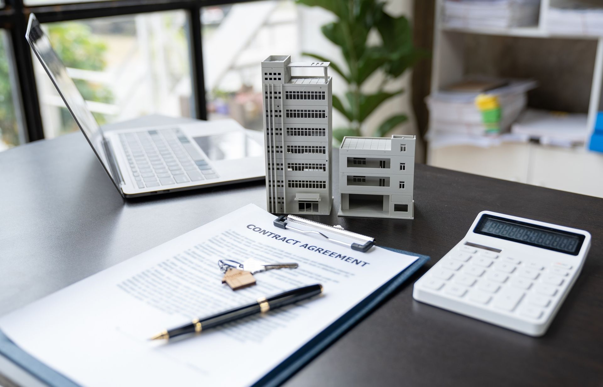 A desk with a laptop , calculator , pen , and model building.