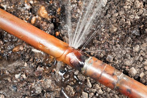 A copper pipe is leaking water on the ground.